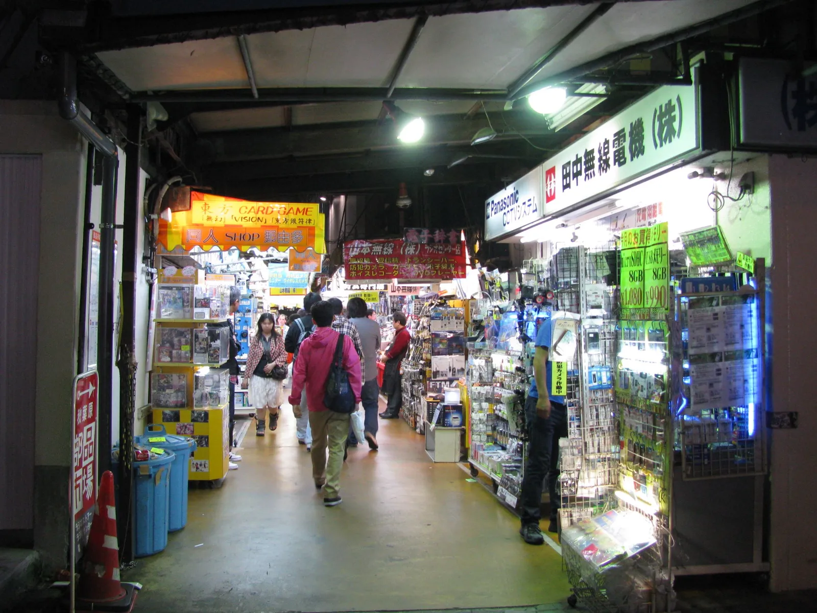 Inside Akihabara Radio Center in Tokyo, a narrow covered passage under the railway lined on both sides with tiny electronics stalls, their shelves and counters packed with components and gadgets under bright signs