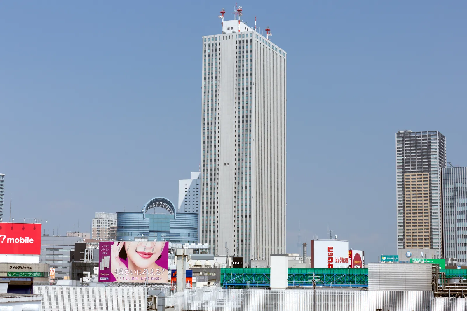 The Sunshine 60 tower in Ikebukuro, Tokyo, a plain white rectangular skyscraper rising high above the lower buildings and rooftops around it under a clear sky