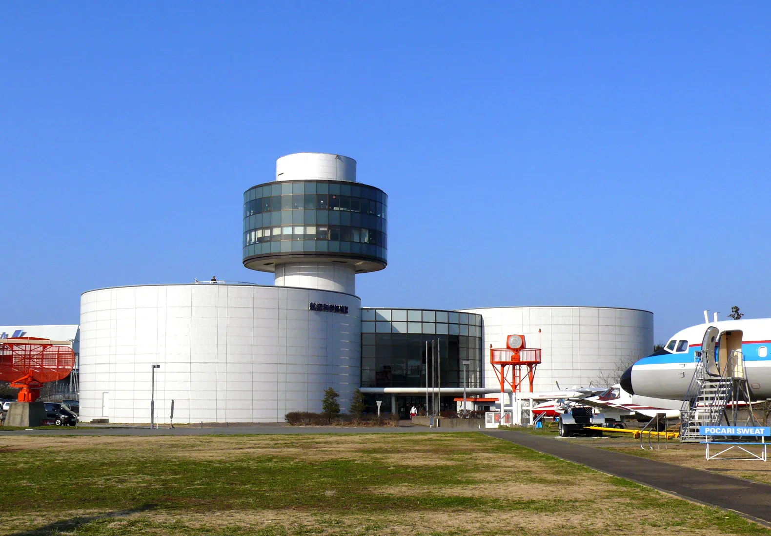 The Museum of Aeronautical Sciences at Shibayama beside Narita Airport, a round white building with a glass-ringed control-tower-style turret on top and a retired passenger jet parked on the grass beside it