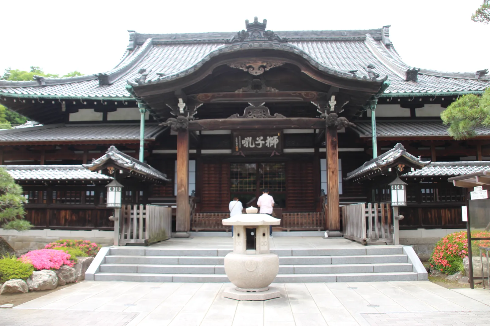 The main hall of Sengaku-ji temple in Takanawa, Tokyo, a broad wooden hall under a grey tiled roof with a curved gable over the entrance steps and a stone incense burner in the paved court in front
