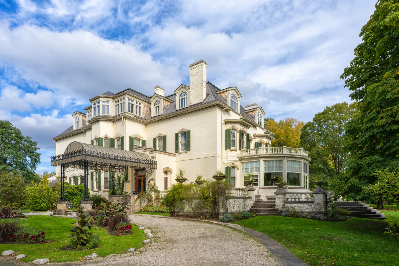 Spadina House in Toronto, a cream-painted Victorian mansion with dormers and a glassed conservatory on one side, seen across a gravel drive and lawns