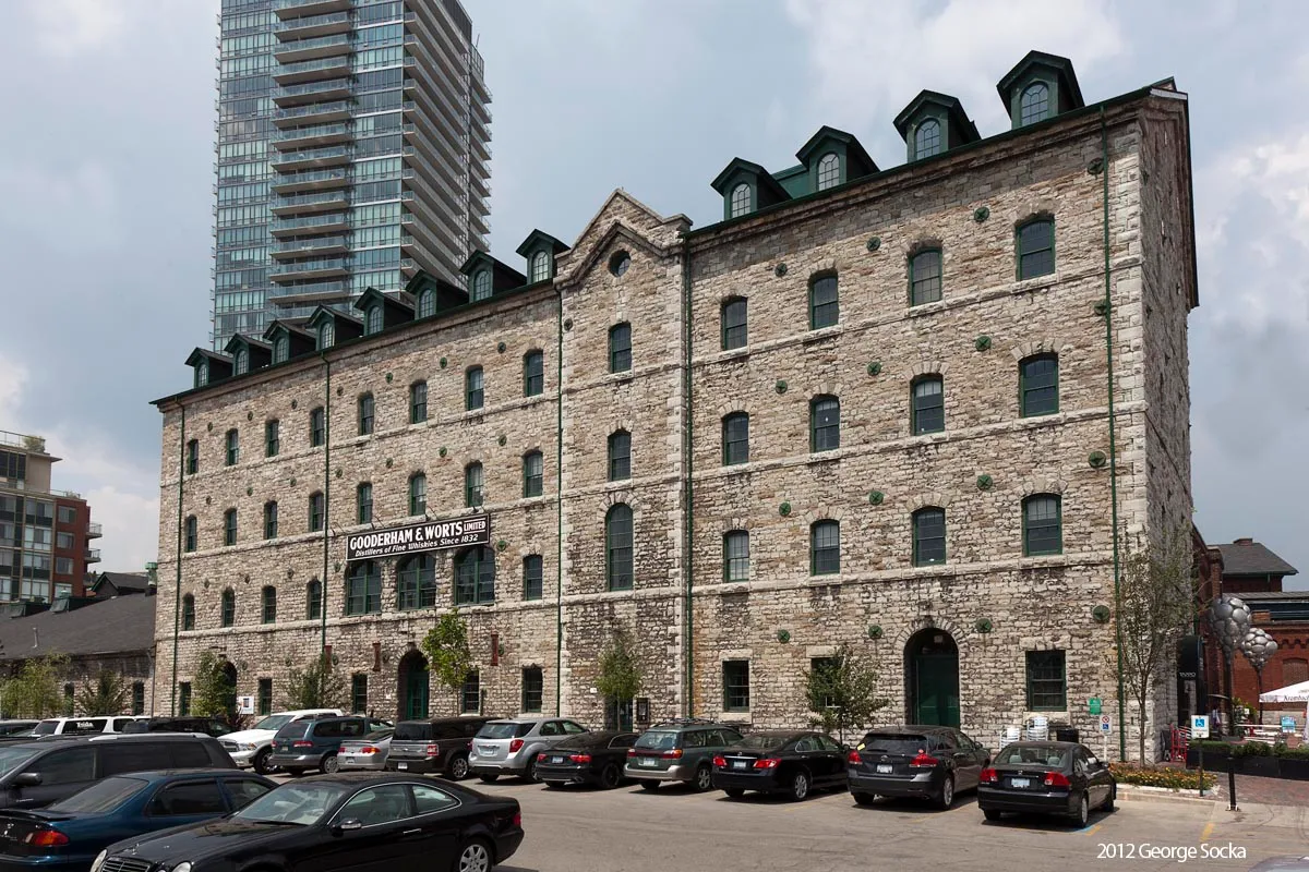The Stone Distillery in Toronto, a five-storey limestone building with rows of small windows and dormers along its roof, a glass condominium tower rising behind it