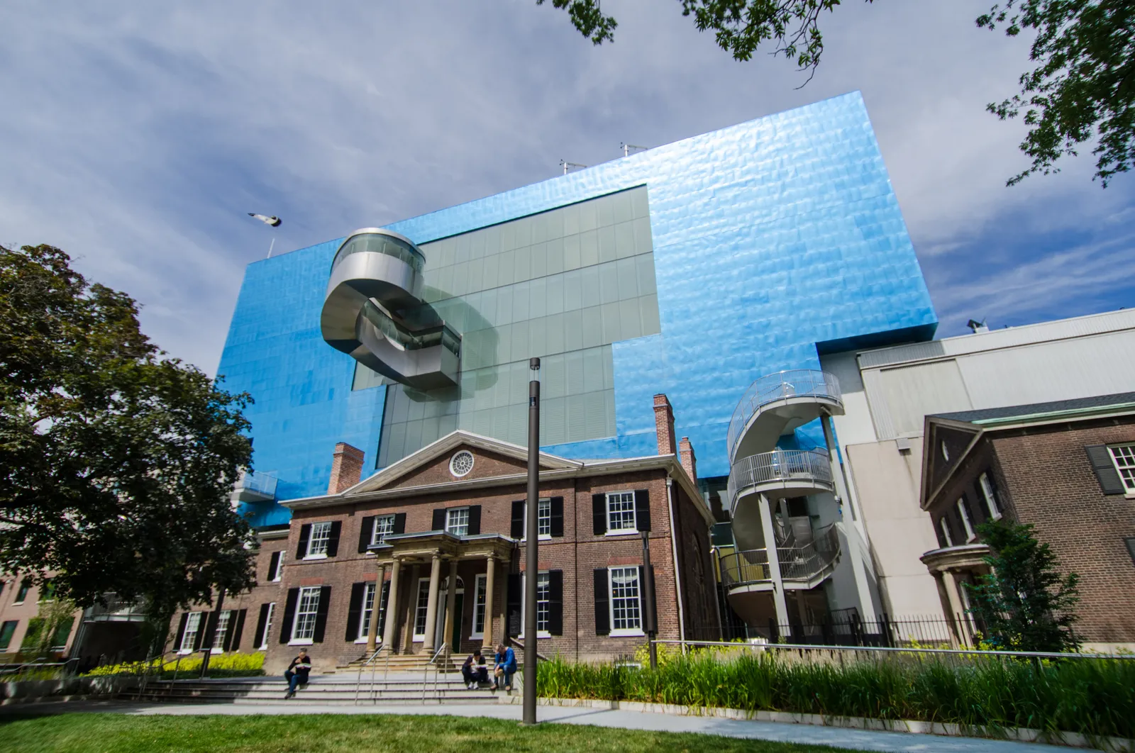 The south side of the Art Gallery of Ontario in Toronto, a blue titanium-clad box cantilevered over a red-brick Georgian house, with a glass staircase spiralling down beside it