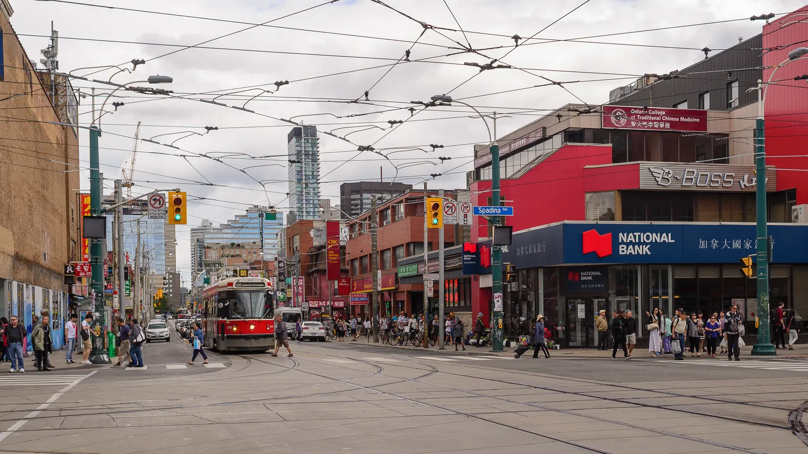 Spadina Avenue in Toronto's Chinatown, a wide street under a web of overhead wires with a red streetcar coming towards the camera and shopfronts signed in Chinese and English on both sides