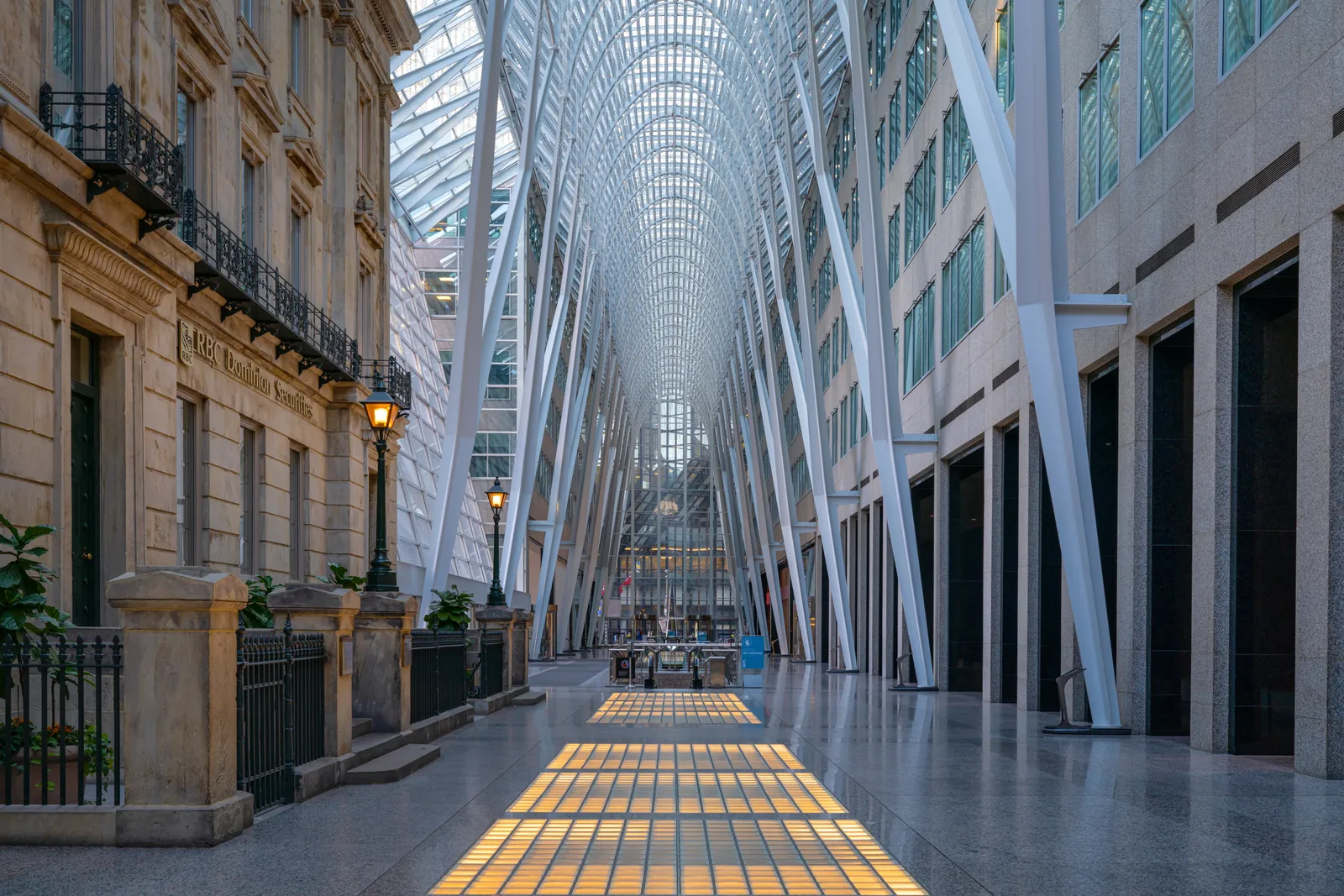 The Allen Lambert Galleria at Brookfield Place in Toronto, a long indoor arcade roofed in glass and held up by tall white steel columns that branch like trees, with a stone heritage facade along the left side