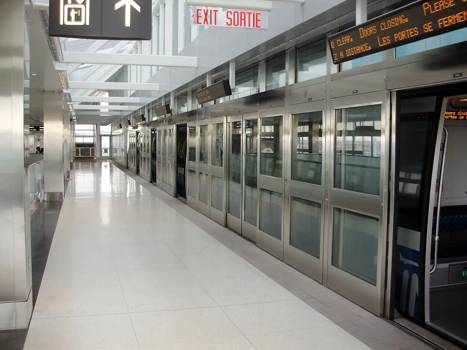 A Link train platform at Toronto Pearson, with glass platform-edge doors along the whole length of the train and bilingual English and French exit signage overhead