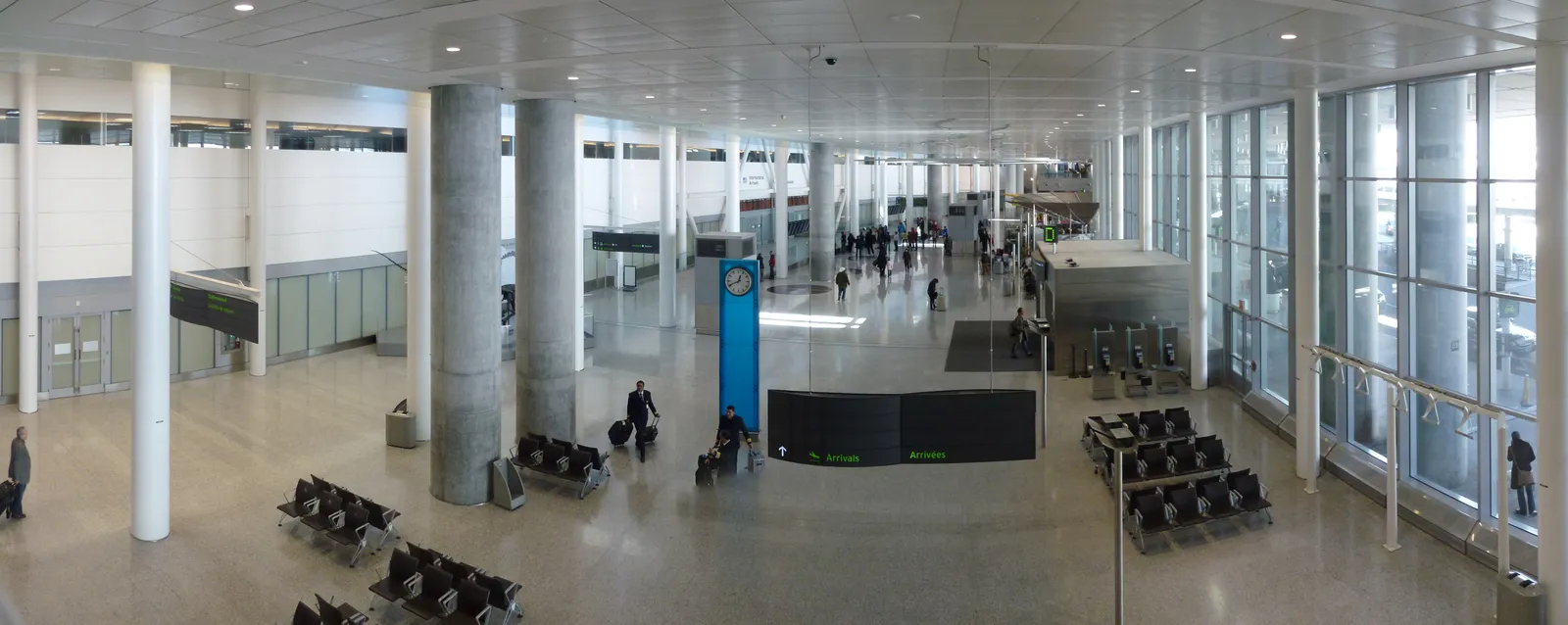 The wide mezzanine level inside Toronto Pearson Terminal 1, a pale concrete and glass hall with rows of seating, tall square columns and daylight coming through the full-height windows on the right