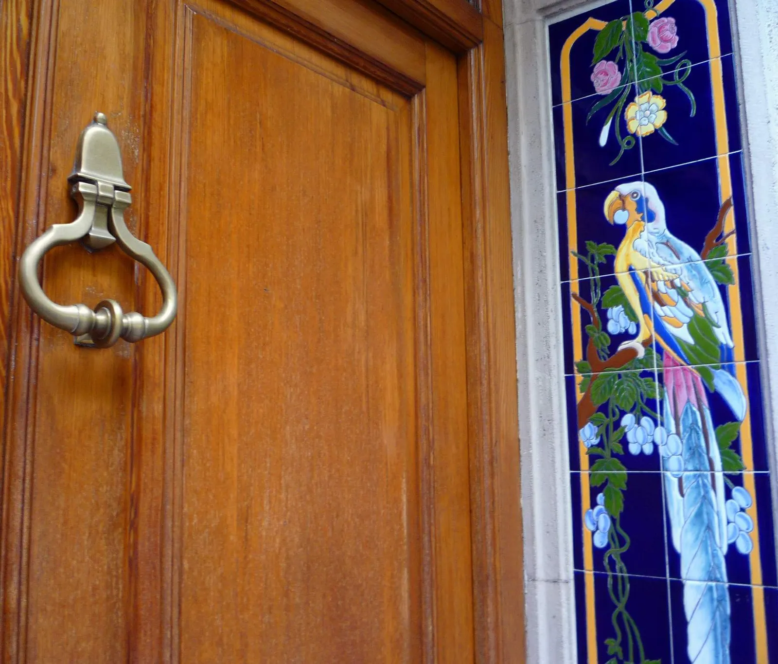A painted tile panel of a parrot on a branch set into the wall beside a varnished wooden front door in Manises
