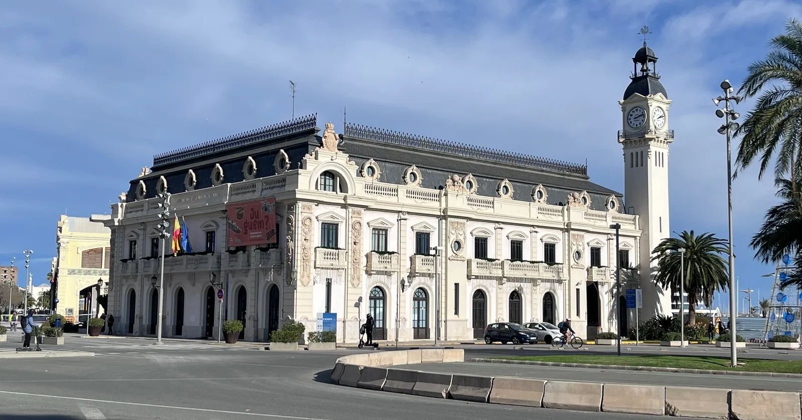 The Clock Building at the Port of Valencia, a long white early twentieth-century block with carved ornament and a tall clock tower at one end, palms in front of it