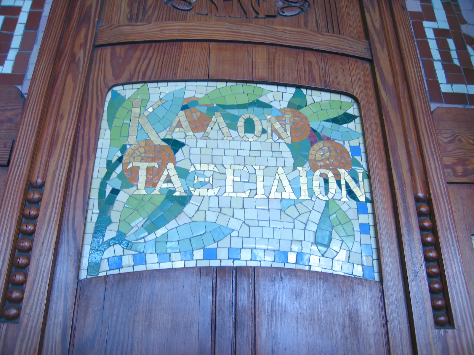 A mosaic panel set into the carved wooden doorway of Estació del Nord in Valencia, reading good journey in Greek letters among orange leaves and fruit