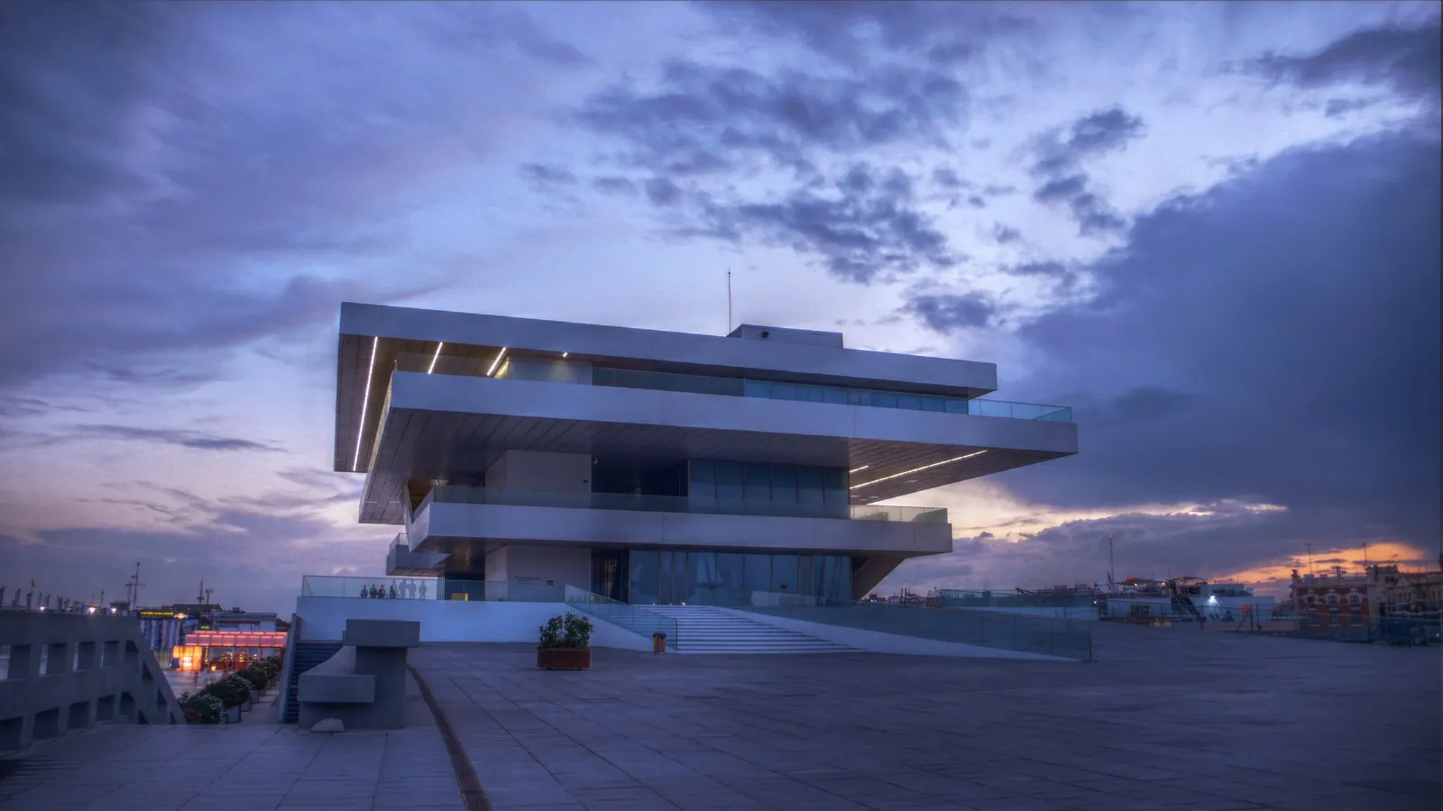 The Veles e Vents building at Valencia's marina at dusk, four stacked white concrete decks cantilevered out over an empty quayside