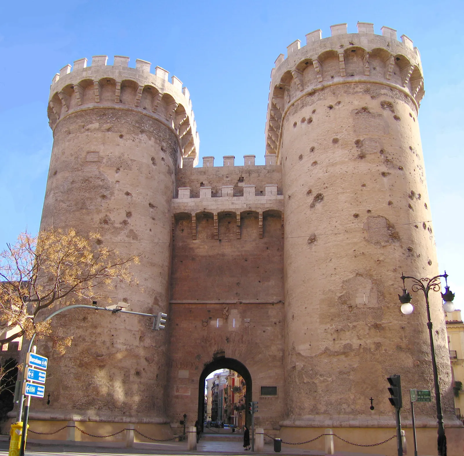 The Torres de Quart in Valencia, two round crenellated towers of pale stone pitted all over with cannonball marks, an archway between them