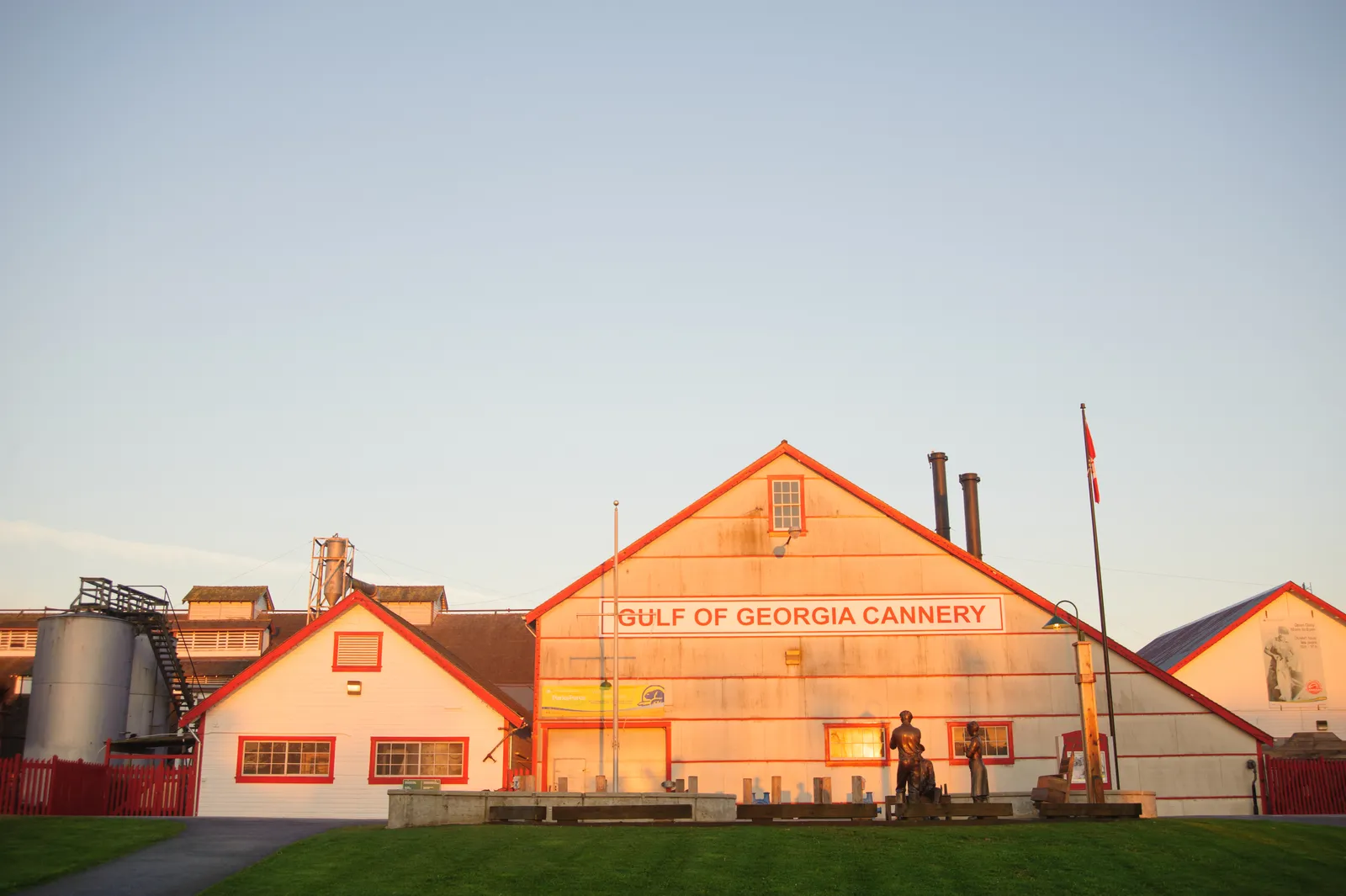 The red-trimmed white gable end of the Gulf of Georgia Cannery National Historic Site in Steveston, its name painted across the facade, with bronze cannery-worker statues on the lawn in front