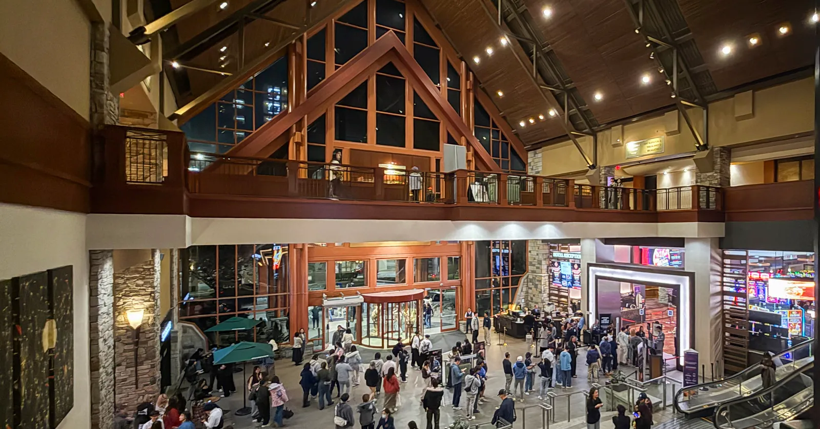 The multi-level timber-framed lobby of River Rock Casino Resort in Richmond, BC, with a crowd queued near the gaming floor entrance and floor-to-ceiling windows behind