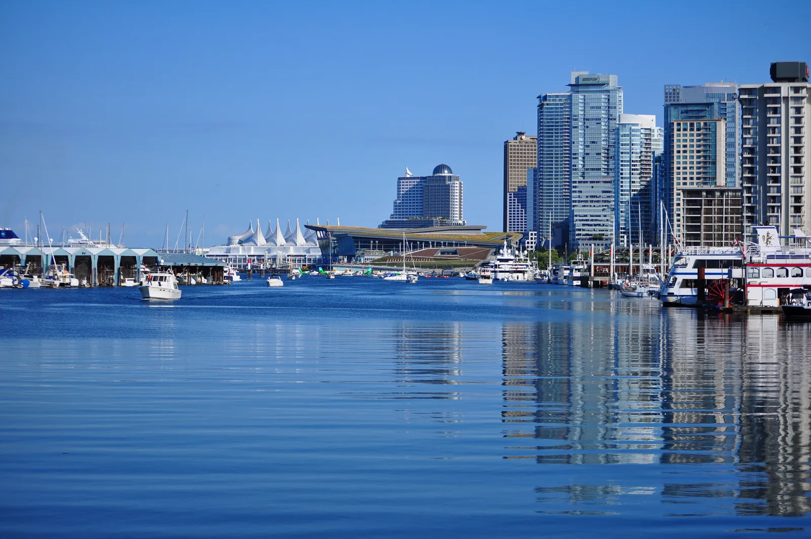 The Vancouver Convention Centre seen along Coal Harbour, its long sloping roof covered in grass, with moored boats in the foreground and downtown towers behind