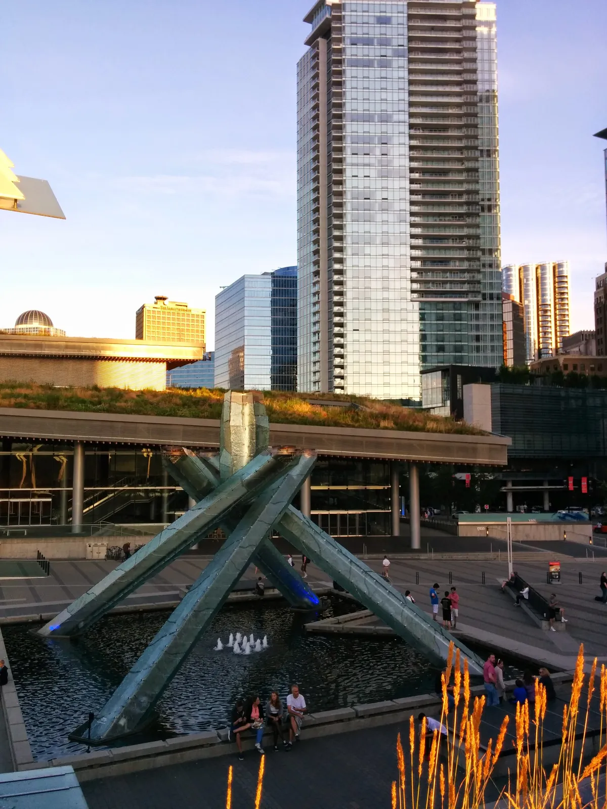 The 2010 Olympic cauldron in Jack Poole Plaza, Vancouver: four angled glass and steel arms crossing over a shallow pool, with the convention centre's planted roof behind it