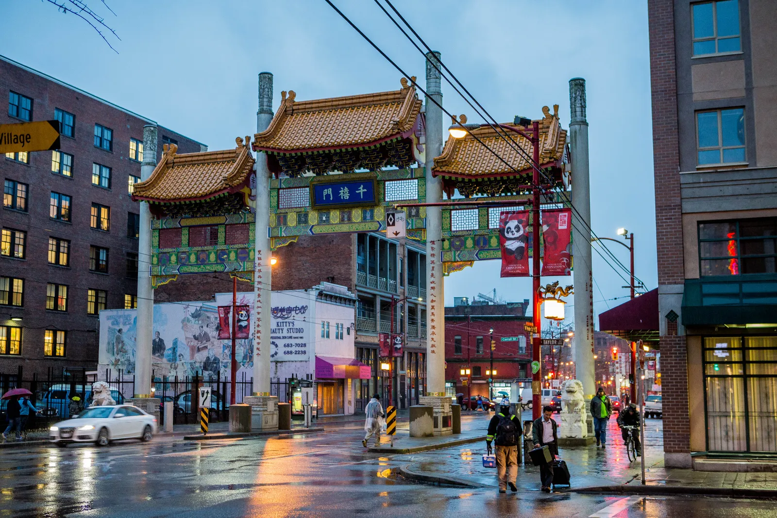 The Millennium Gate spanning Pender Street in Vancouver's Chinatown at dusk in the rain, its three tiled roofs lit up above the wet road