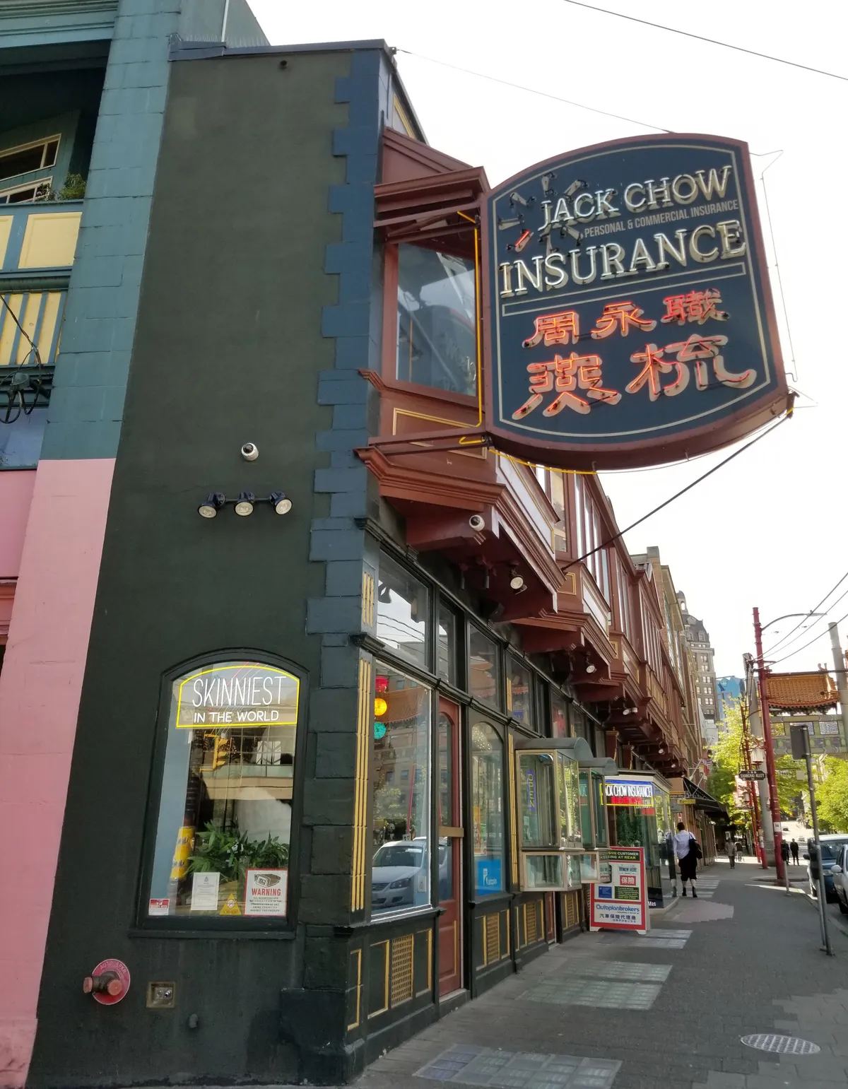 The Sam Kee Building on West Pender Street in Vancouver seen along its length, its dark end wall barely wider than a doorframe and a row of copper bay windows running back down the block