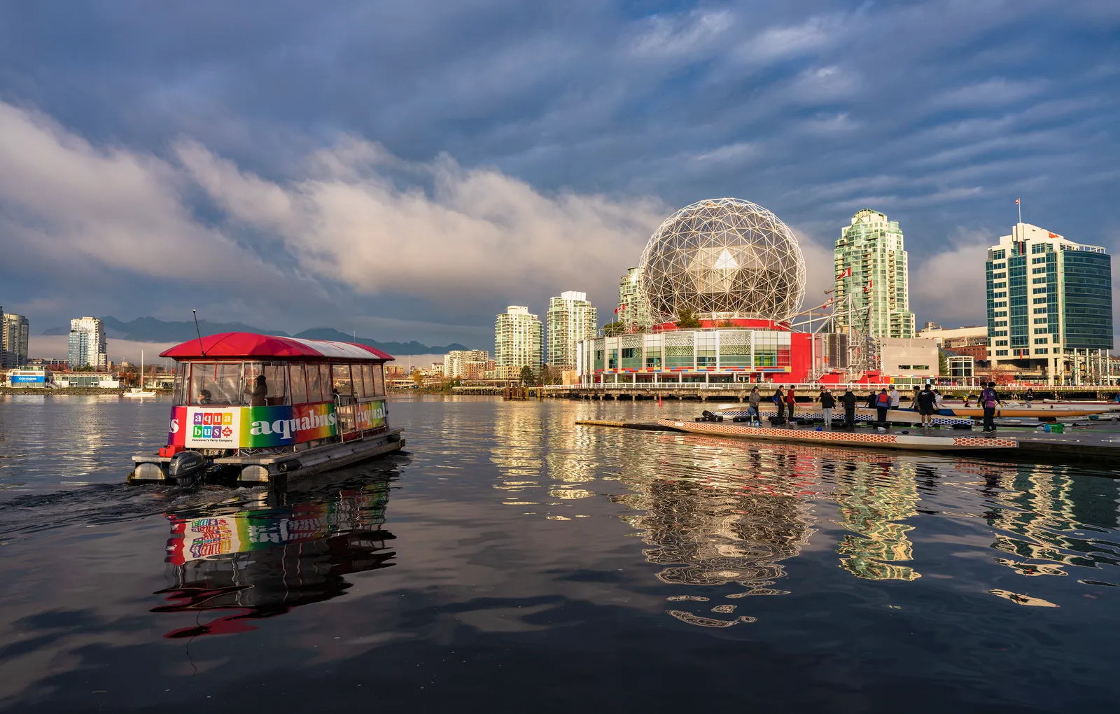 The silver geodesic dome of Science World at the eastern end of False Creek in Vancouver, with a small covered ferry crossing the water in front of it
