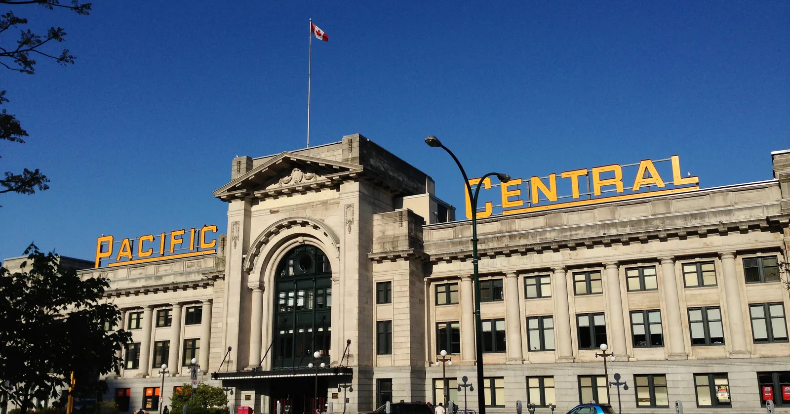The pale stone Beaux-Arts facade of Pacific Central Station in Vancouver under a clear sky, with the words PACIFIC CENTRAL in yellow letters along the roofline