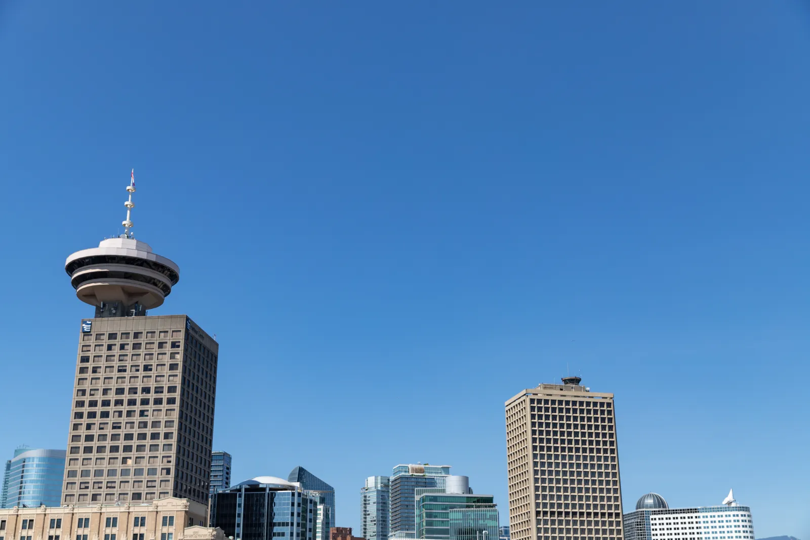 The saucer-shaped observation deck of the Harbour Centre tower in Vancouver rising above the downtown office blocks against a clear blue sky