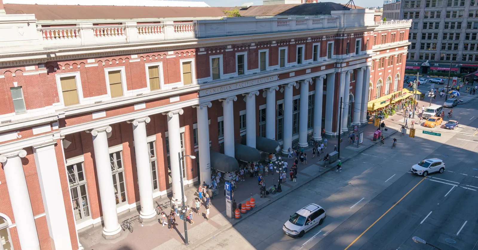 The red-brick facade of Waterfront Station in Vancouver seen from above Cordova Street, with its row of white Ionic columns and people waiting under the awning