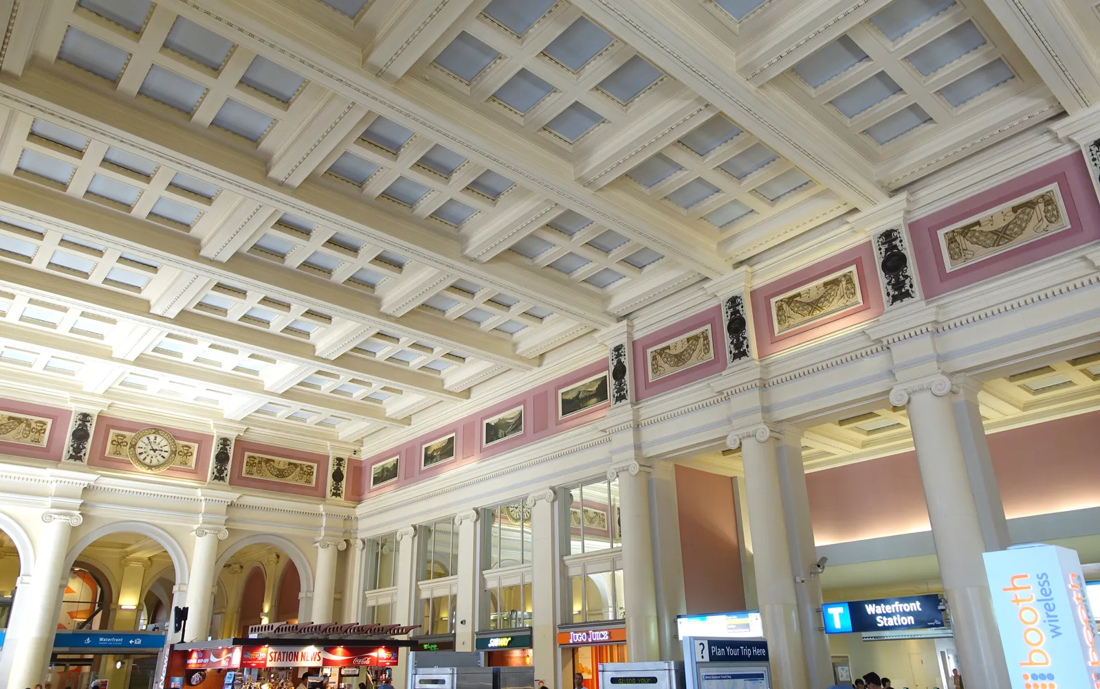 The coffered ceiling and white columns of the main hall inside Waterfront Station in Vancouver, with painted panels running above the cornice