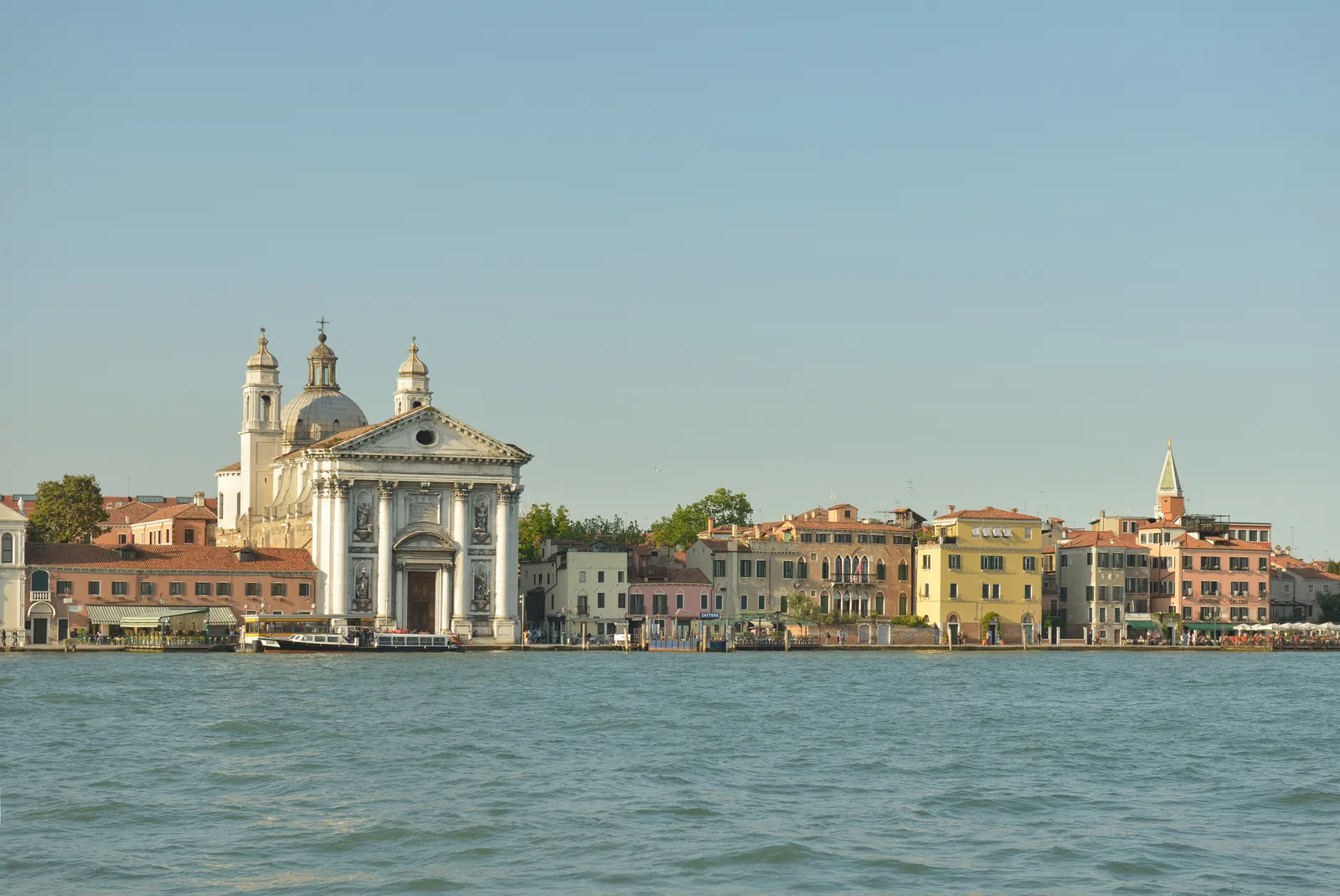 The Zattere waterfront in Dorsoduro seen across the Giudecca Canal, with the domed Chiesa dei Gesuati and colorful buildings along the promenade