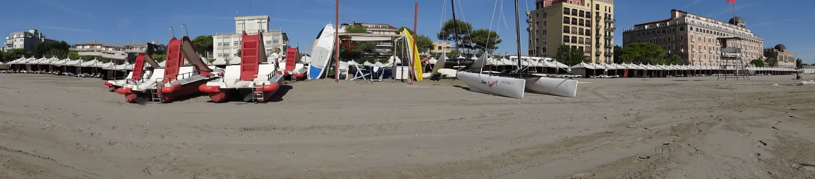 The sandy beach on Venice's Lido island with paddle boats and sailboats pulled up on the sand and hotels along the shorefront