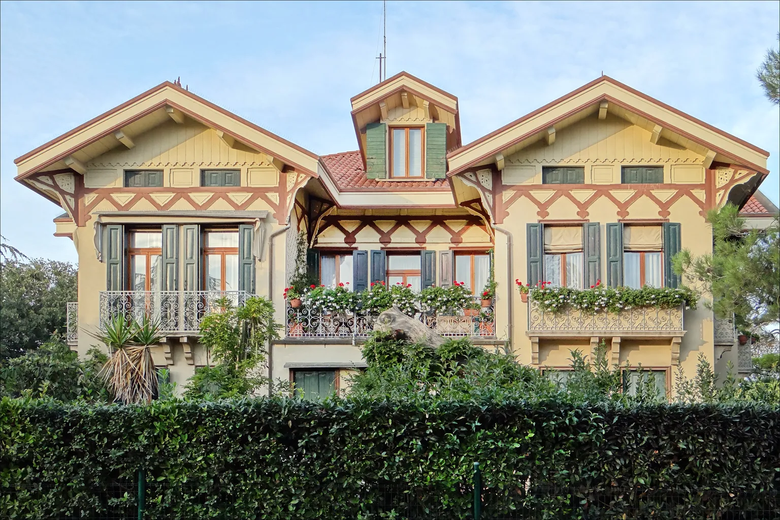 Villa Elena on the Lido, a yellow and red Liberty-style timber-gabled house with flower-filled balconies