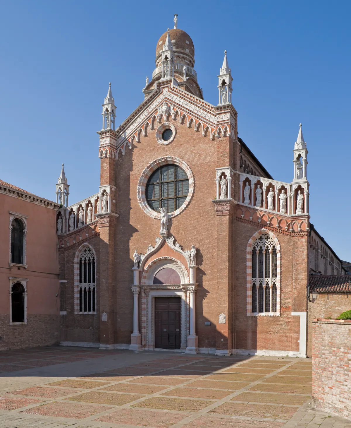 The red-brick Gothic front of the church of Madonna dell'Orto in Venice's Cannaregio district, with a rose window, a row of statues and an onion-domed bell tower behind