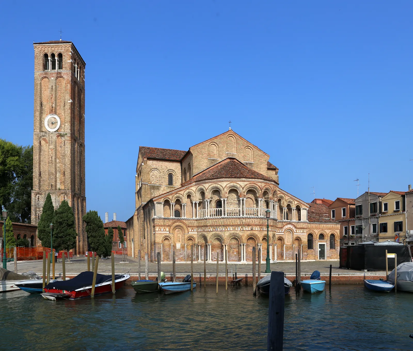 The basilica of Santi Maria e Donato on Murano, its brick apse wrapped in two tiers of arcading with slender marble columns, beside a detached brick bell tower with a clock face
