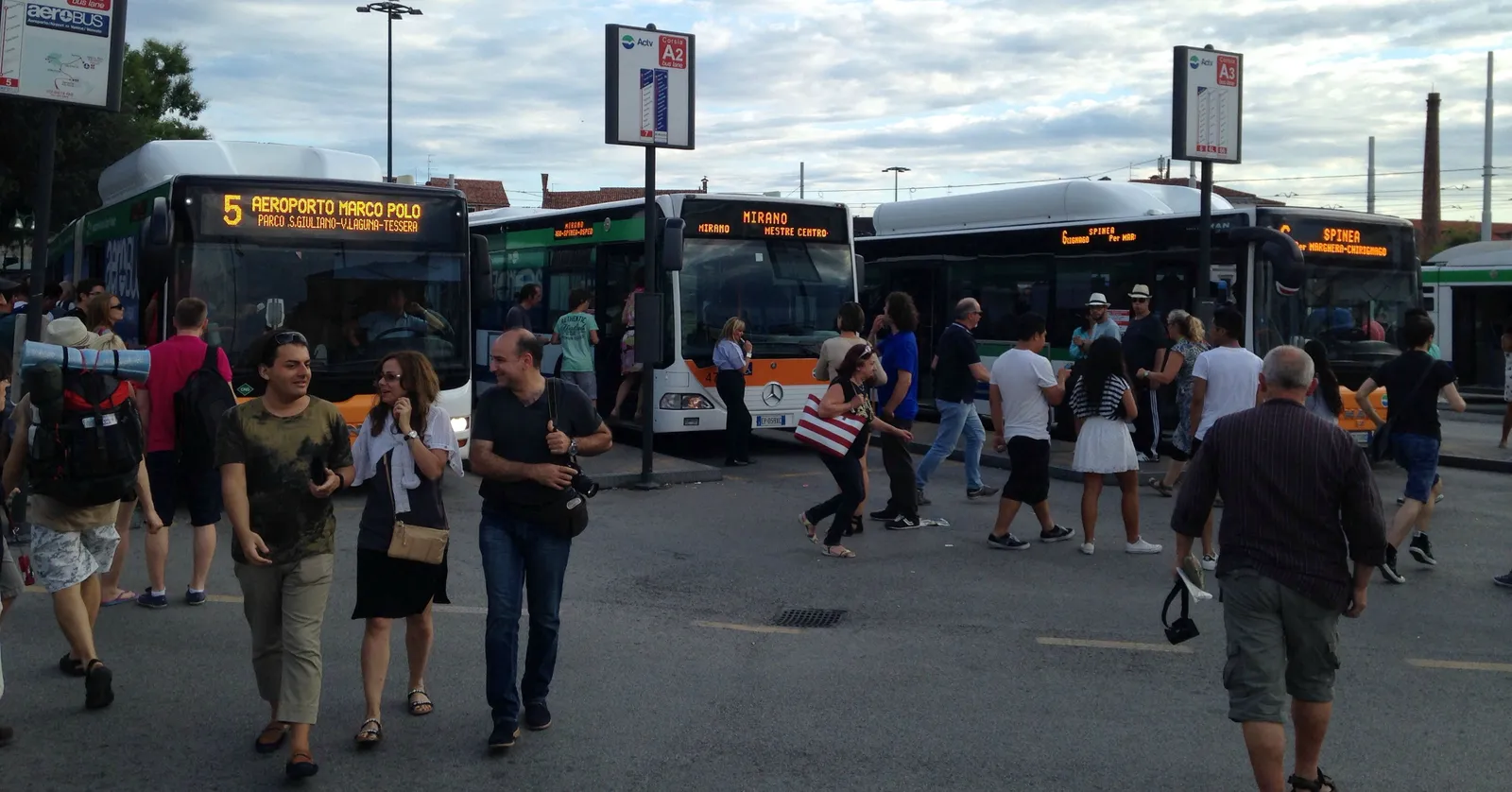 Buses lined up along the kerb at Piazzale Roma in Venice, the nearest one showing AEROPORTO MARCO POLO on its destination board, with passengers walking across the open paving in front of them