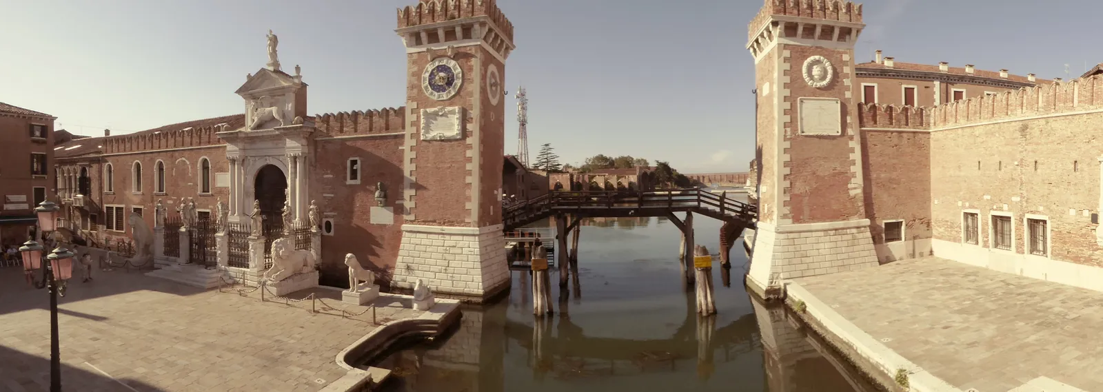 The fortified brick land gate of the Venetian Arsenale with twin crenellated towers and stone lion statues, reflected in the water