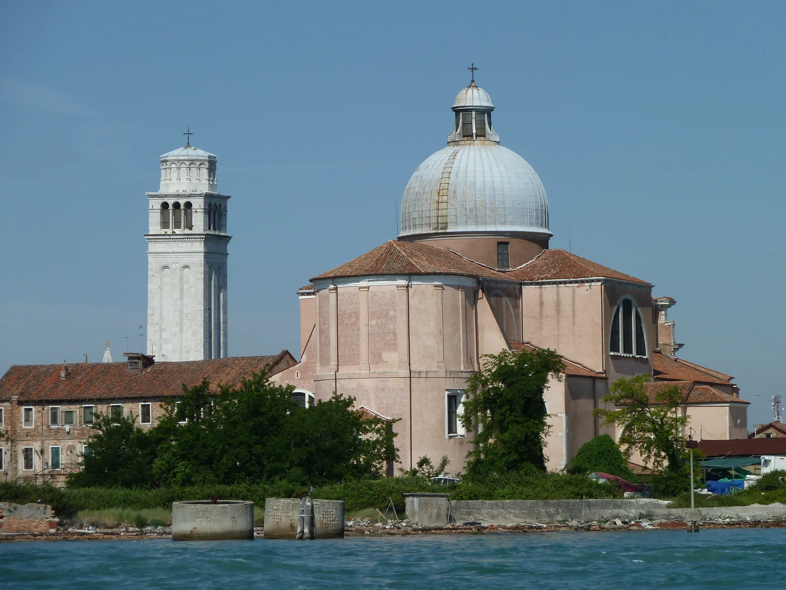 The basilica of San Pietro di Castello in Venice seen across the water, a wide grey dome over a pale brick church, with a separate white stone bell tower leaning slightly to one side beside it