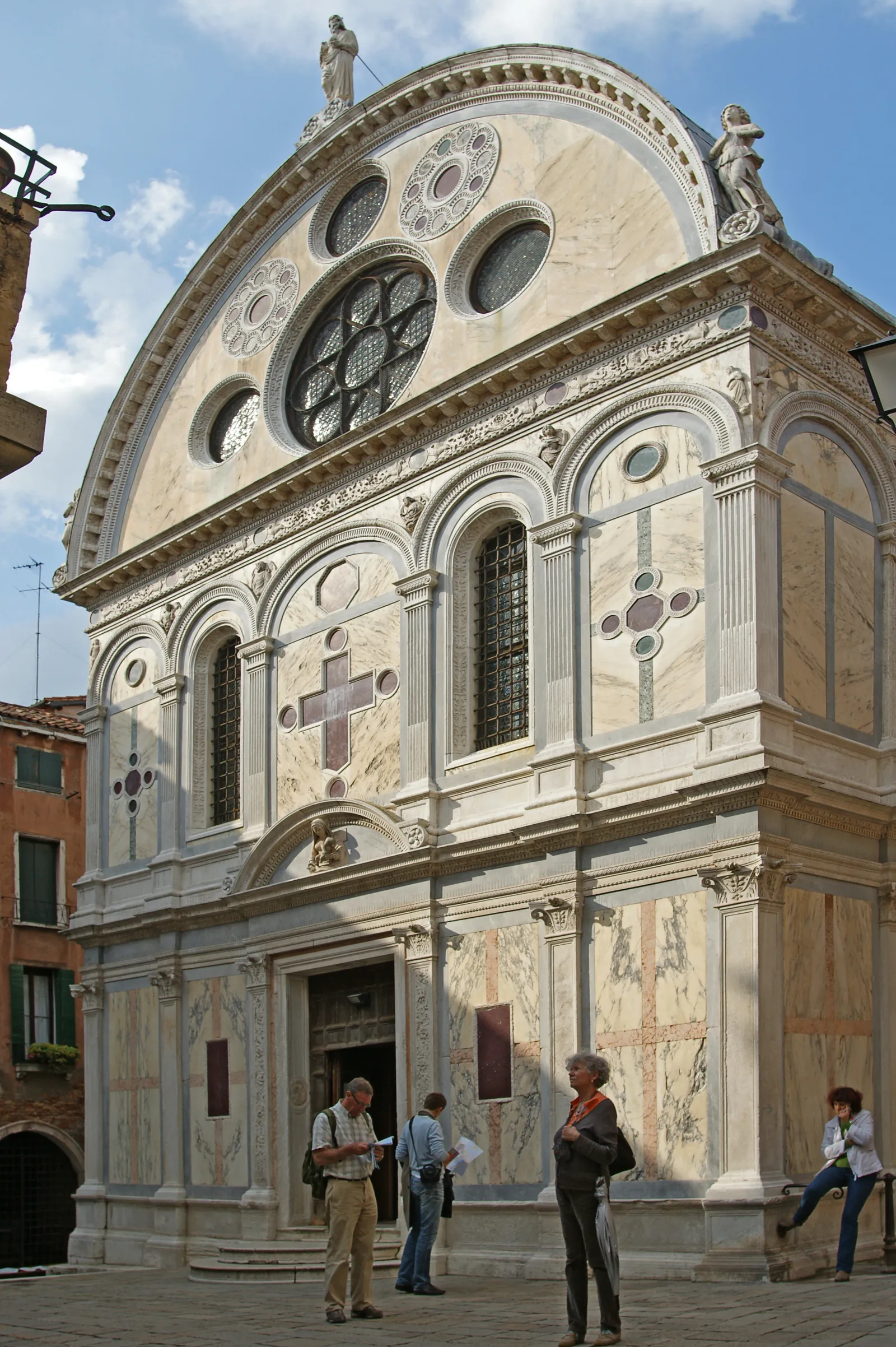 The front of Santa Maria dei Miracoli in Venice, a small church faced entirely in panels of pale and coloured marble, with round windows set into a semicircular gable above the door