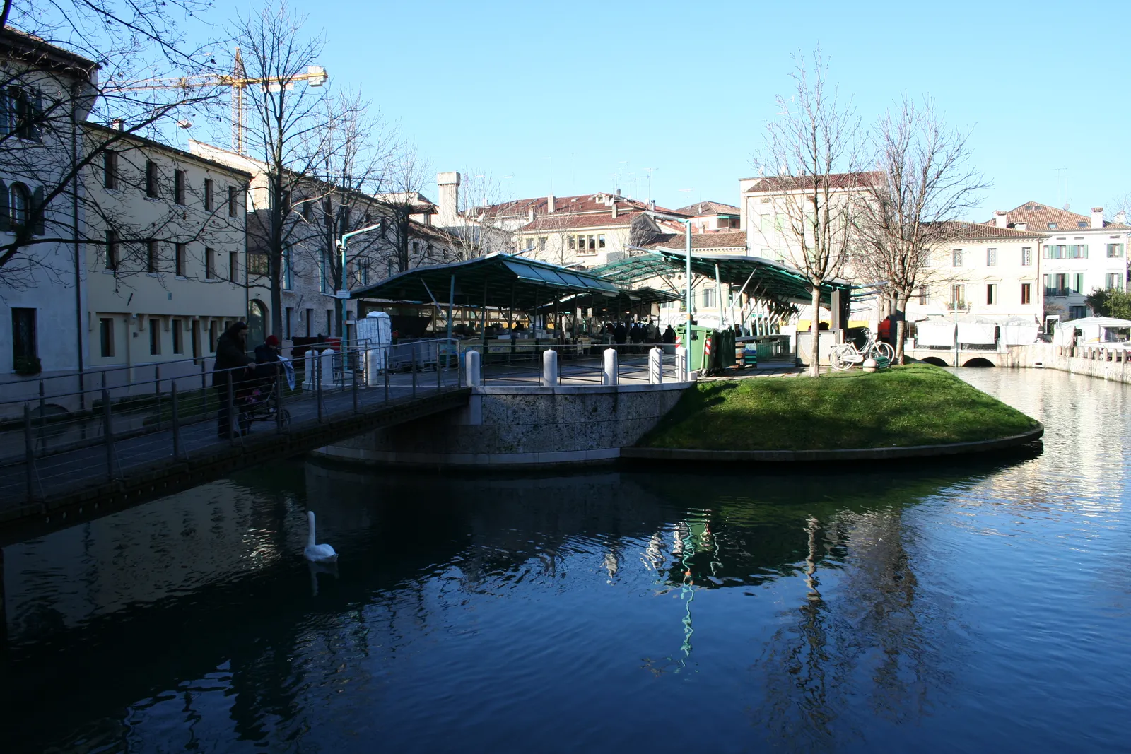 The Isola della Pescheria in Treviso, a small island in the middle of a canal carrying the green-roofed fish market stalls, with a footbridge onto it and arcaded buildings along the bank behind