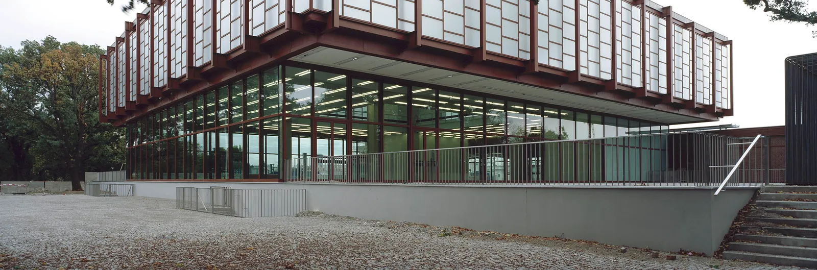 The Belvedere 21 in Vienna, a long single-storey modernist pavilion of glass walls under a projecting slatted roof, set on a gravel forecourt among trees