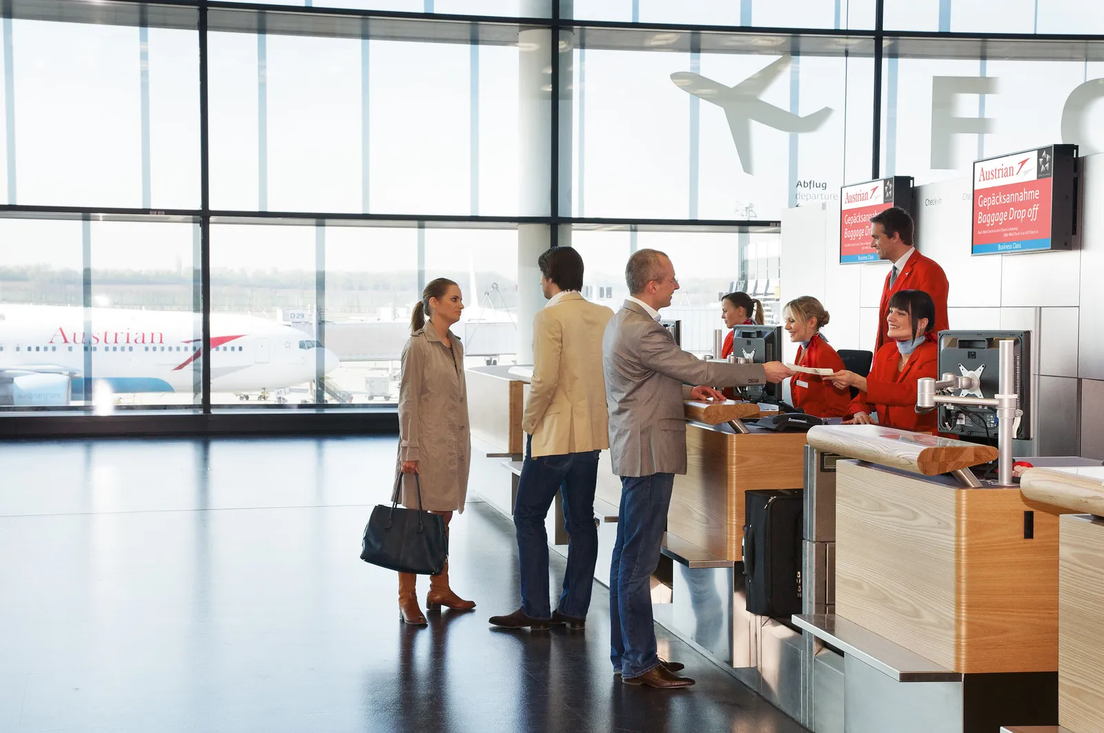 The check-in area inside Terminal 3 at Vienna Airport, passengers at a staffed desk with a full-height window behind them looking out to aircraft parked on the apron