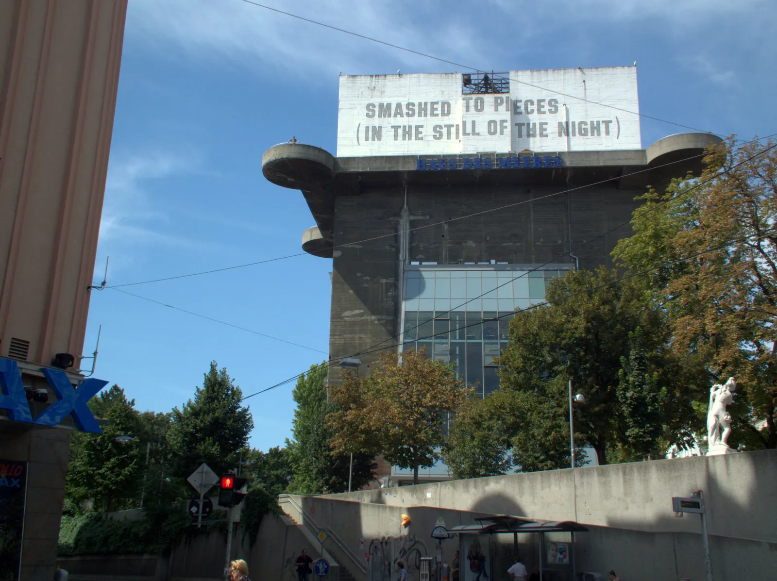 The concrete anti-aircraft tower in Vienna's Esterhazypark, a windowless grey wartime block with projecting gun platforms near the top, now carrying a glass extension and a text artwork across its upper wall