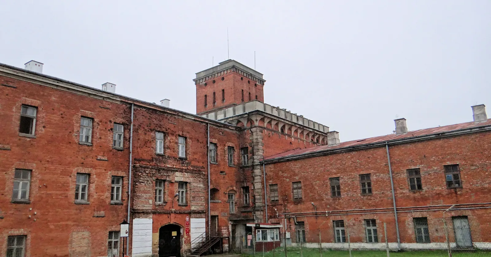 The Red Tower at Modlin Fortress, a square red brick observation tower rising above the two-storey brick barracks ranges that enclose the yard in front of it