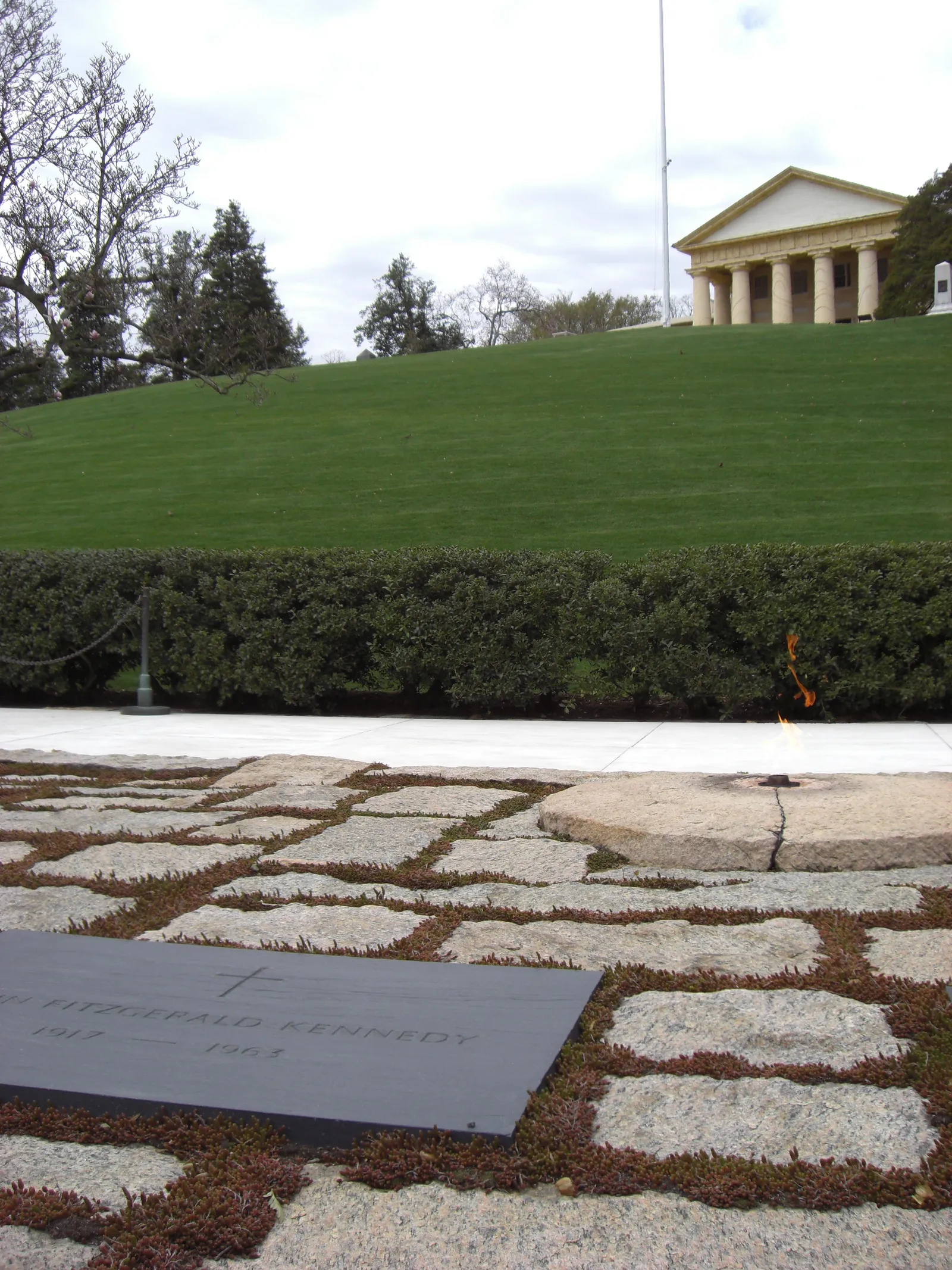 The Kennedy gravesite at Arlington, a flagstone terrace with the eternal flame burning at its centre and the columned portico of Arlington House on the grass slope above