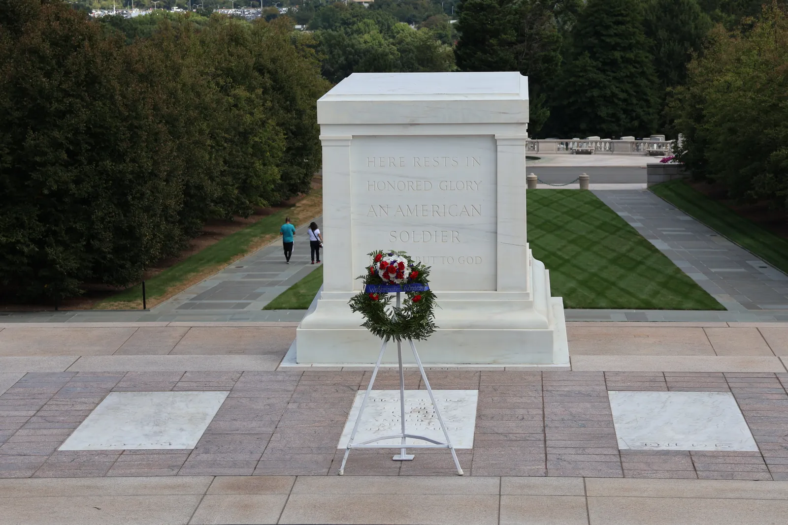 The Tomb of the Unknown Soldier at Arlington National Cemetery, a white marble sarcophagus carrying its carved inscription, with a wreath standing in front of it on the plaza