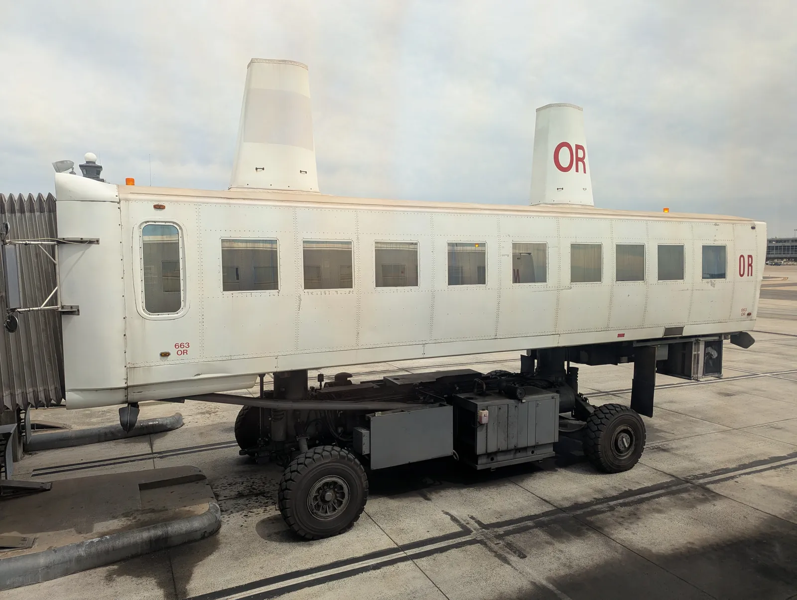 A mobile lounge at Washington Dulles, a long white windowed cabin raised on a wheeled chassis, standing on the apron beside the terminal