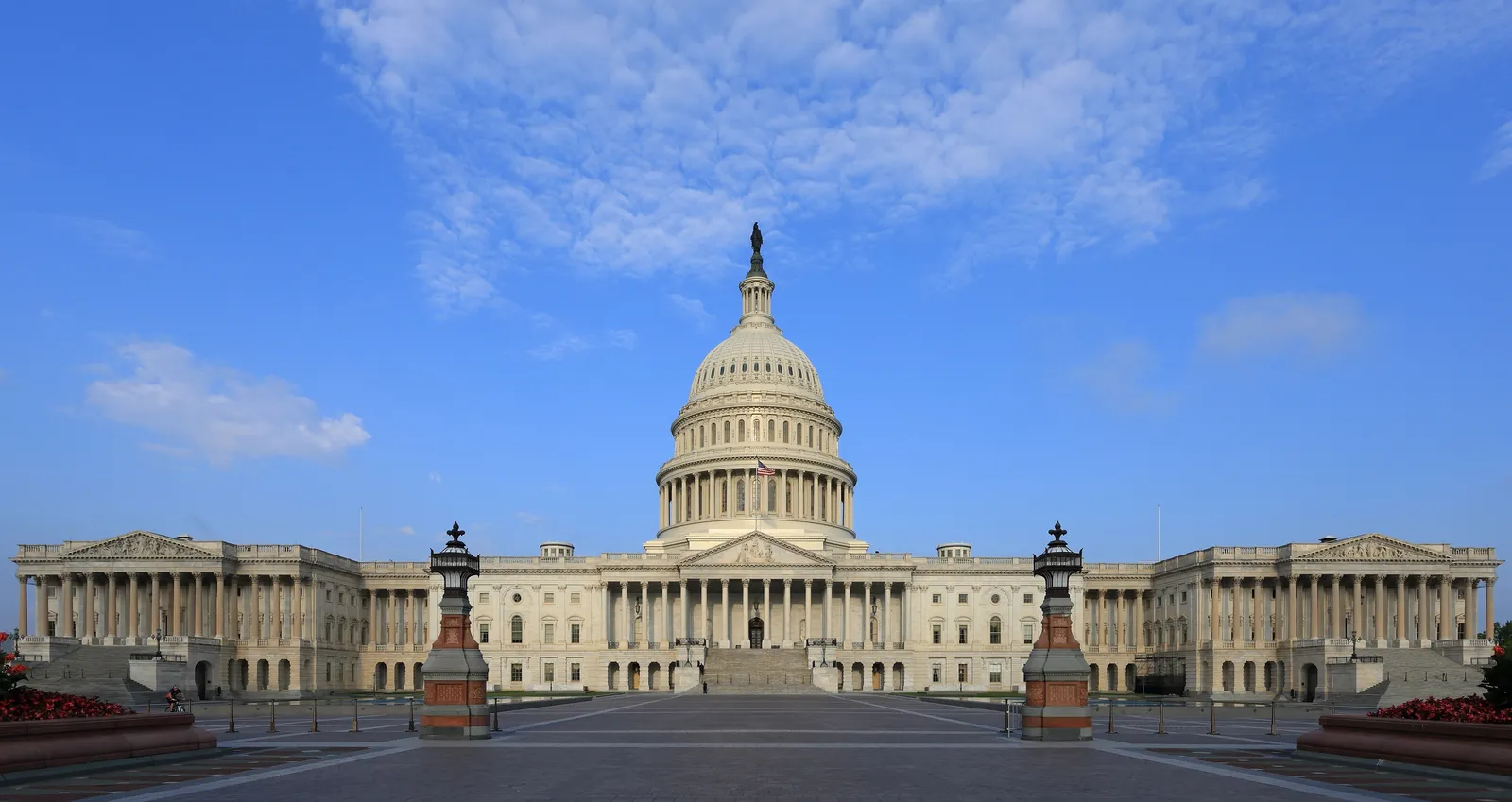 The east front of the United States Capitol in Washington, its dome above a symmetrical sandstone and marble facade, seen across the paved plaza in front