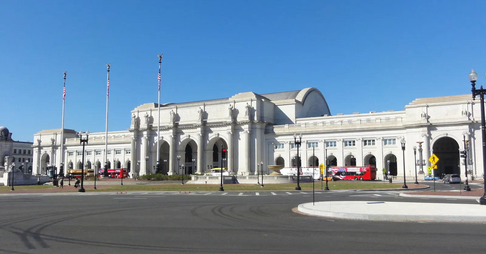 The white granite front of Washington Union Station under a clear sky, a long arcaded facade with a curved roof rising behind it and flagpoles along the plaza